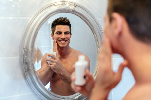 Healthy positive male treating sking with lotion after shaving